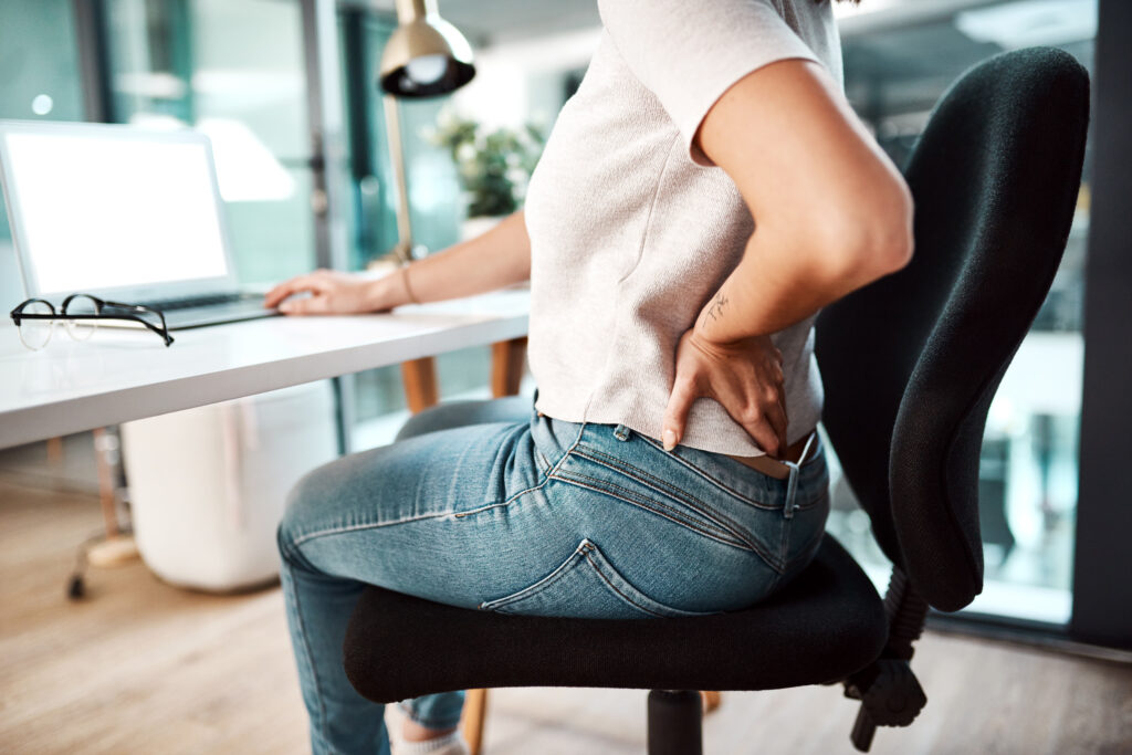 Office worker holding lower back in pain, highlighting the impact of sedentary desk work.