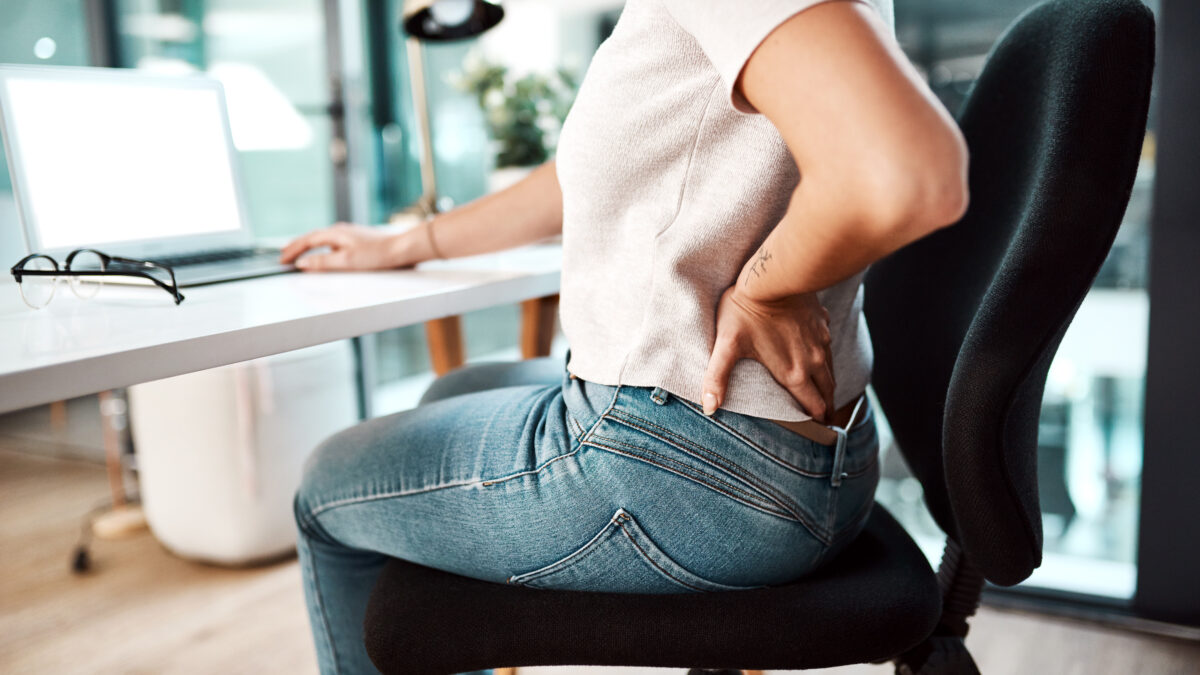 Office worker holding lower back in pain, highlighting the impact of sedentary desk work.