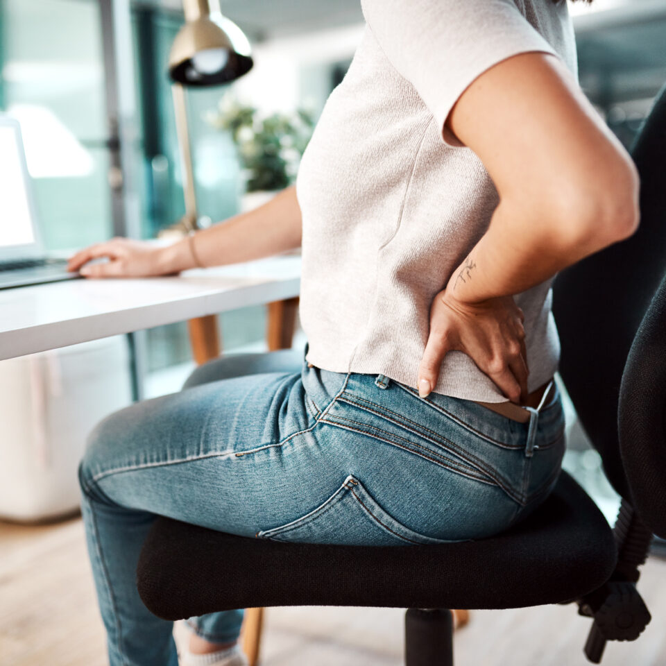 Office worker holding lower back in pain, highlighting the impact of sedentary desk work.