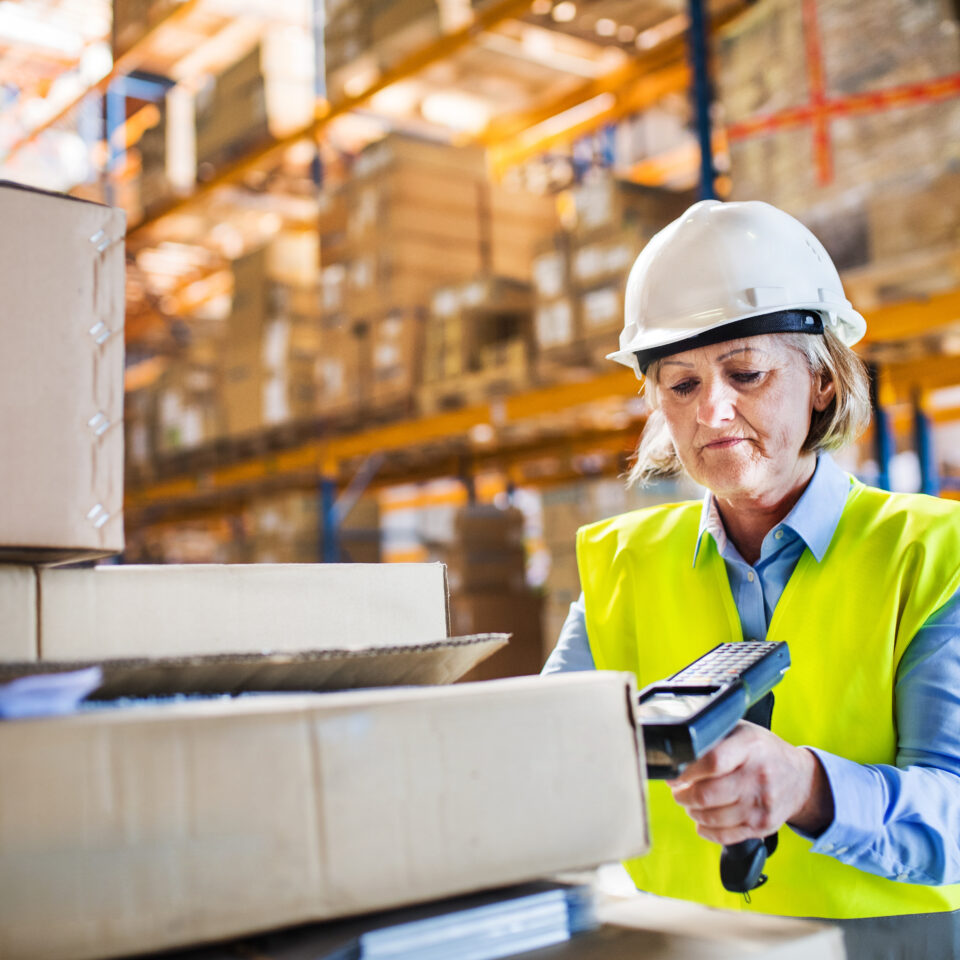 Senior warehouse woman worker or supervisor using a mobile handheld PC with barcode scanner.