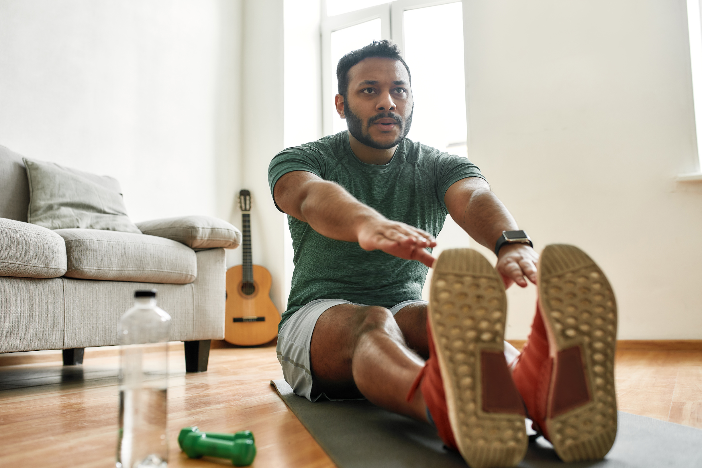 Do your best. Young active man watching online video training during morning workout with dumbbells on yoga mat at home. Sport, healthy lifestyle. Horizontal shot