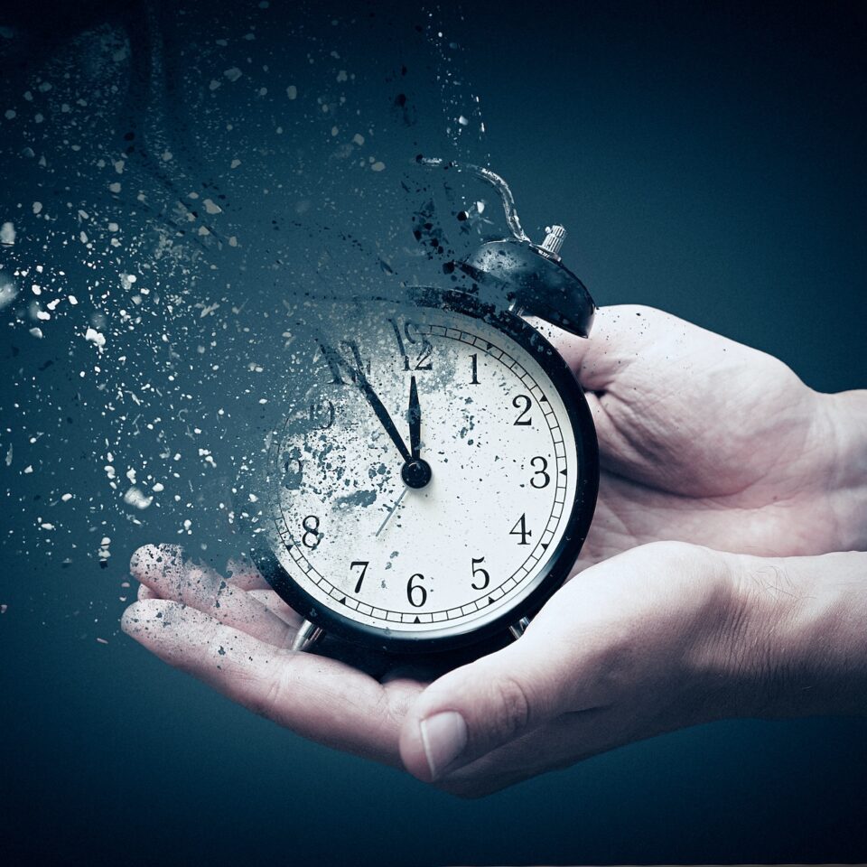 Concept of passing away, the clock breaks down into pieces. Hand holding analog clock with dispersion effect