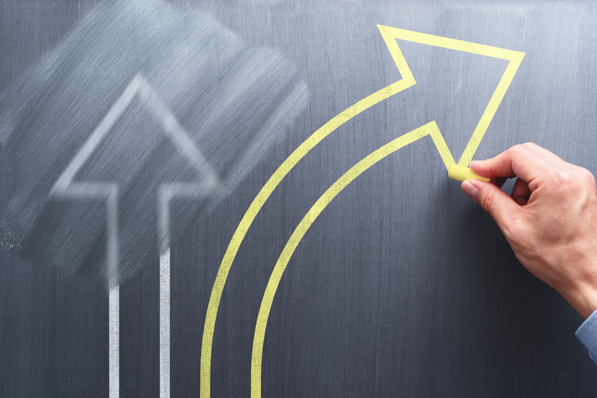 Hand drawing a yellow arrow curving upward on a chalkboard, symbolising a positive change in direction or improvement in workplace injury prevention strategy.