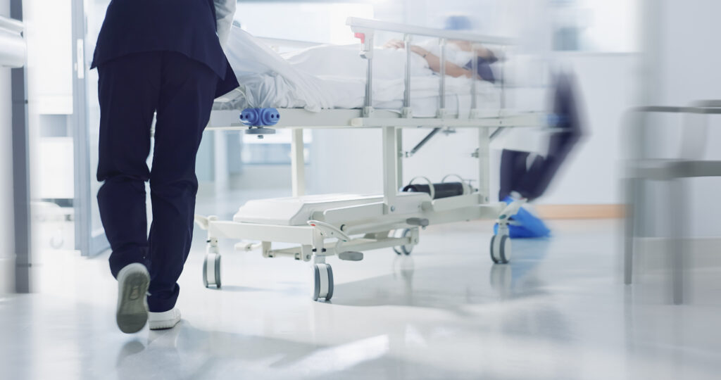 Healthcare workers pushing a hospital bed down a corridor, symbolising the pace, strain, and urgency faced by clinical frontline teams.