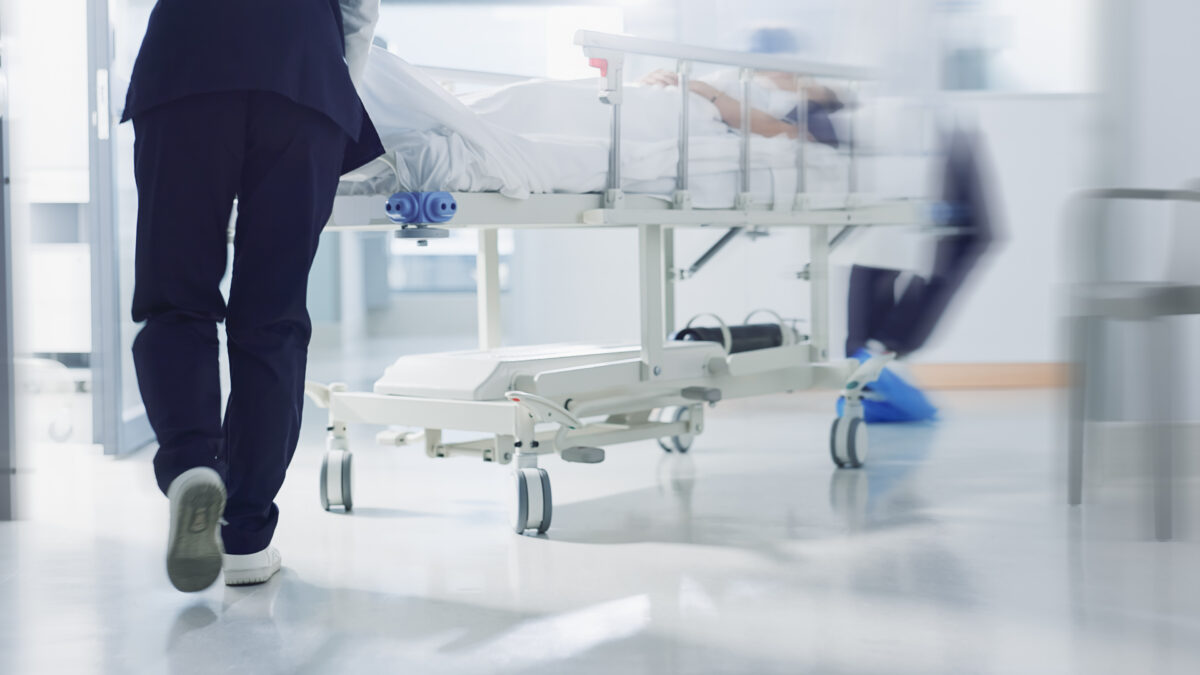 Healthcare workers pushing a hospital bed down a corridor, symbolising the pace, strain, and urgency faced by clinical frontline teams.