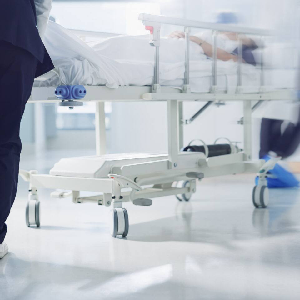 Healthcare workers pushing a hospital bed down a corridor, symbolising the pace, strain, and urgency faced by clinical frontline teams.