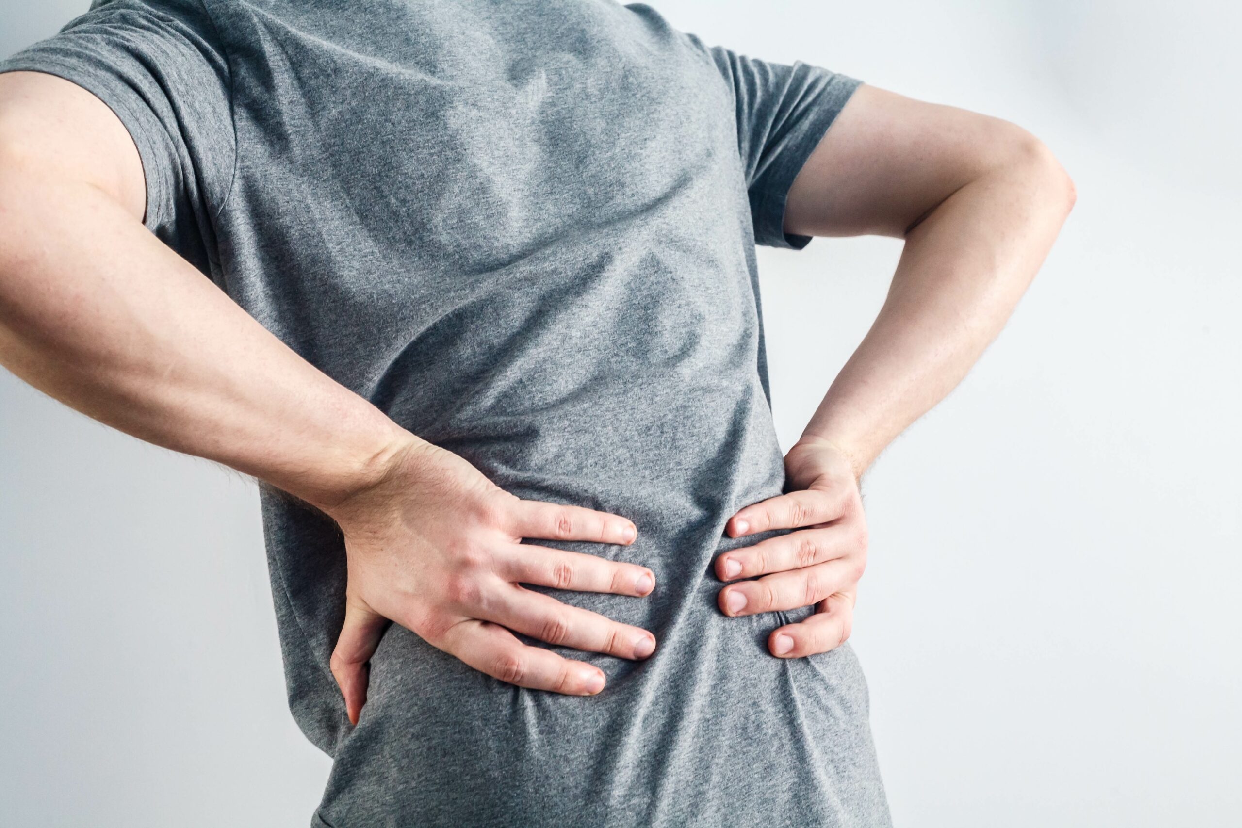 A worker holds their lower back, suggesting discomfort or pain. This visual represents the early physical symptoms of work-related musculoskeletal disorders (MSDs), commonly experienced in manual handling roles.