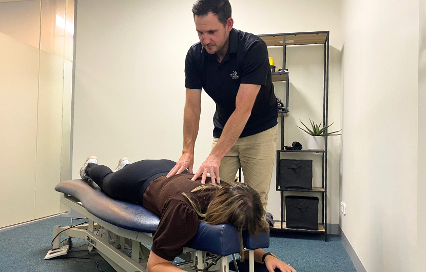 Clinician providing manual therapy to a worker lying face down in an onsite treatment room.